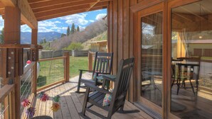 A wooden deck with a view of mountains, a wooden chair, and a table.