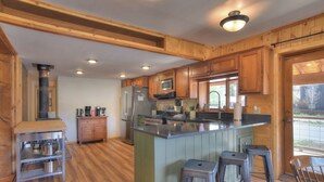 A kitchen with wooden cabinets, a stainless steel refrigerator, a microwave, and a stove. There are stools and a bar stool near the counter.