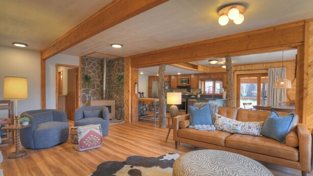 A cozy living room with a stone fireplace, wooden beams, a sofa, and a cowhide rug.