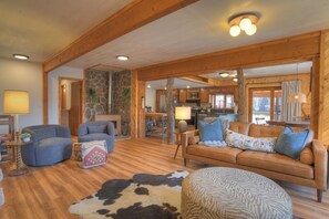 A cozy living room with a stone fireplace, wooden beams, a sofa, and a cowhide rug. - New Listing! Walkable to Downtown Creede | Mountain Views | OHV's Welcome (Creede)