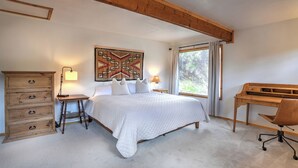 A bedroom with a bed, dresser, desk, and a window with curtains.