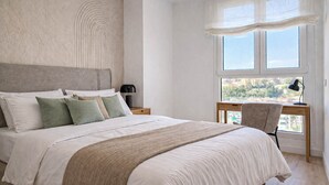 Une chambre avec un grand lit, un bureau avec une chaise, une fenêtre donnant sur un beau paysage et une lampe sur la table de chevet.