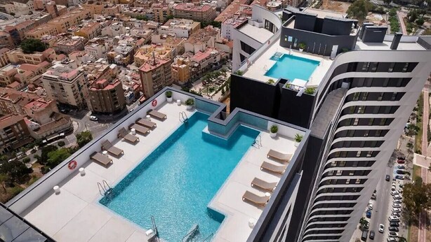 Une piscine sur le toit, dotée de chaises longues et offrant une vue sur le paysage urbain.
