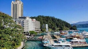 A marina with boats docked, a tall building, and a forested hillside. - Island Heart Sun Moon Lake Hotel (Yuchi)