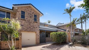 A two-story brick house with a garage, a covered patio, and a fenced yard with palm trees.