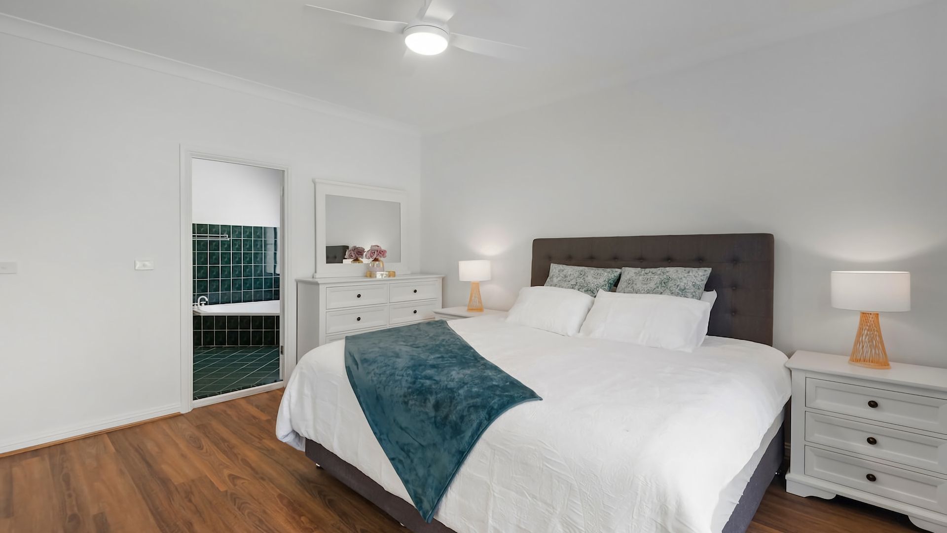 A bedroom with a bed, nightstands, a dresser, a mirror, and a bathroom with a bathtub.