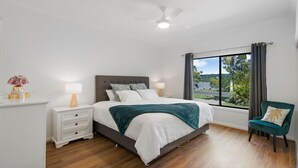 A bedroom with a bed, bedside tables, a chair, a window with a view, and a ceiling fan. - Robins Place - Pet Friendly River Retreat (Empire Vale)