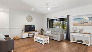 A modern living room with a sofa, TV, coffee table, and a painting of a beach scene. - Robins Place - Pet Friendly River Retreat (Empire Vale)