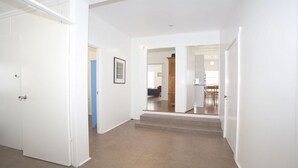 A hallway with white walls, a blue door, and a staircase leading to a dining area. - My Blue Heaven Dog Friendly (Lennox Head)