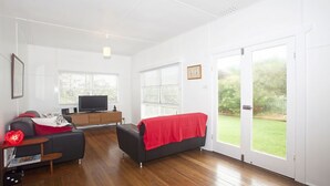 A modern living room with a flat-screen TV, a sofa, a red blanket, and a wooden cabinet. - My Blue Heaven Dog Friendly (Lennox Head)