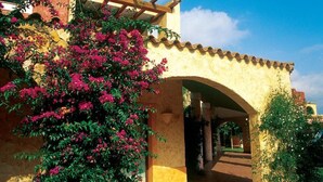 Ein Gebäude mit gelber Fassade, einem Rundbogen-Eingang und einer Pergola mit Kletterpflanzen.