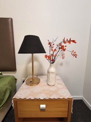 Een nachtkastje met een lamp en een vaas met takken.