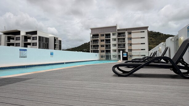 A rooftop pool area with lounge chairs, a swimming pool, and modern buildings in the background.
