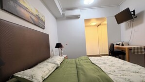 A bedroom with a bed, a desk, a chair, a TV, and an air conditioning unit.