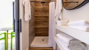 Ein modernes Badezimmer mit Dusche, Holzwand, weißen Ablagen mit Handtüchern und einem Spiegel.