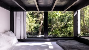 Ein Schlafzimmer mit großem Fenster, einem Bett und Blick auf einen Wald.