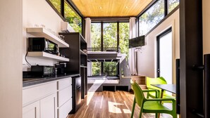 Eine moderne Küche mit integriertem Ofen, Mikrowelle und Kaffeemaschine, ein Essbereich mit Tisch und Stühlen und große Fenster mit Blick auf Grünflächen.