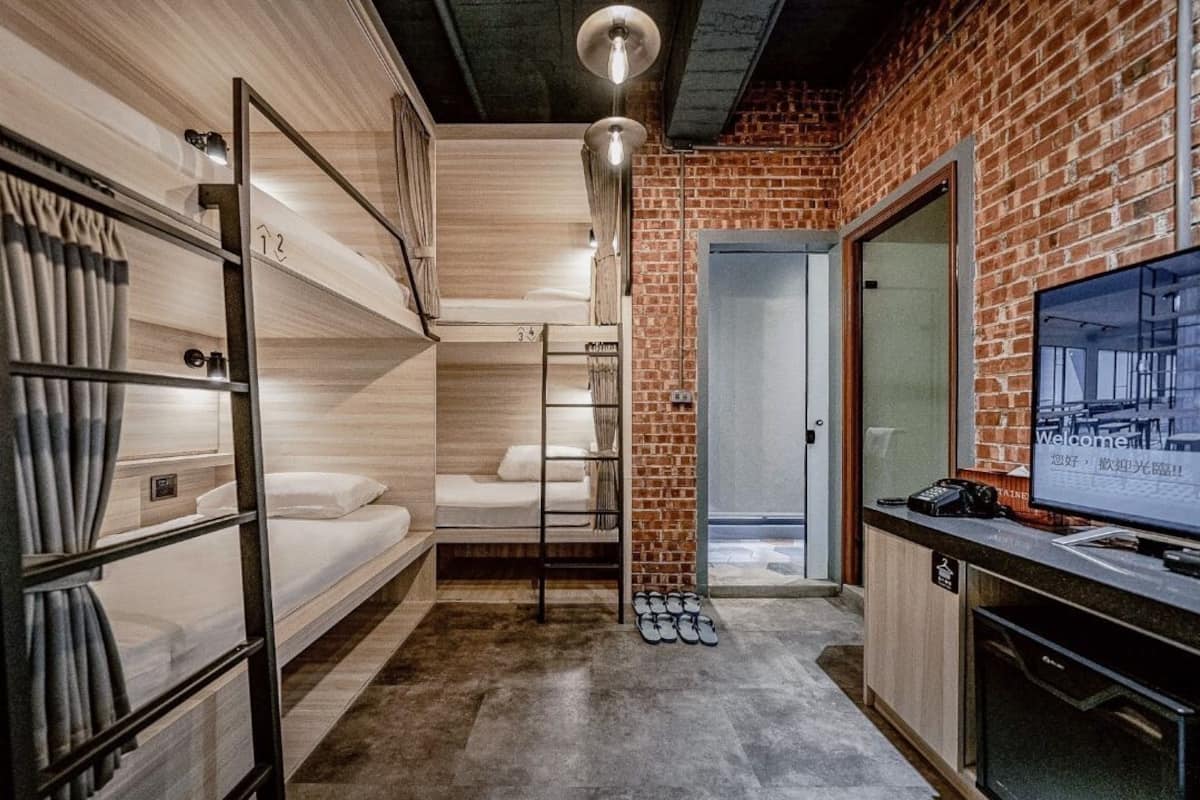 Habitación de hotel con literas, un escritorio, una televisión y una pared de ladrillo.