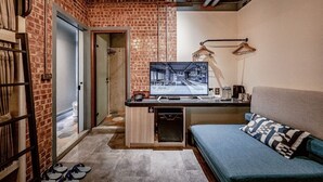 Quarto com parede de tijolos, uma escrivaninha com monitor de computador, um sofá e um lustre.