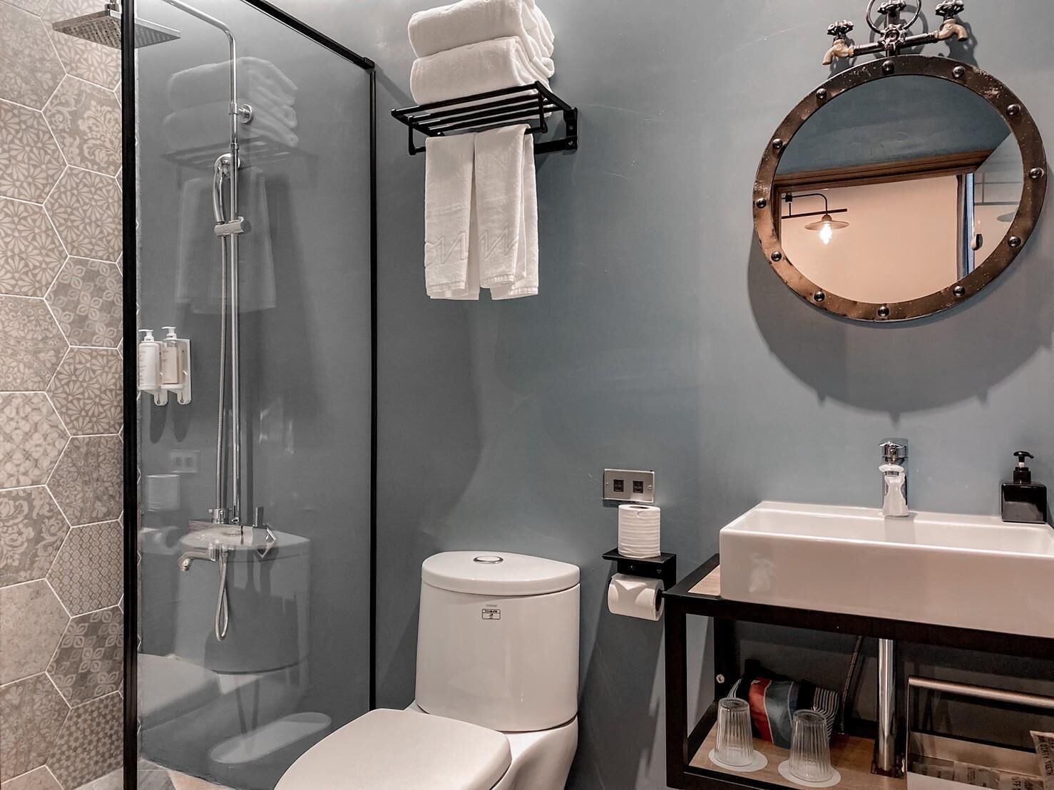 Un baño moderno con cabina de ducha de vidrio, inodoro, lavamanos con espejo y toallero.