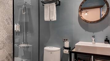 Un baño moderno con cabina de ducha de vidrio, inodoro, lavamanos con espejo y toallero.