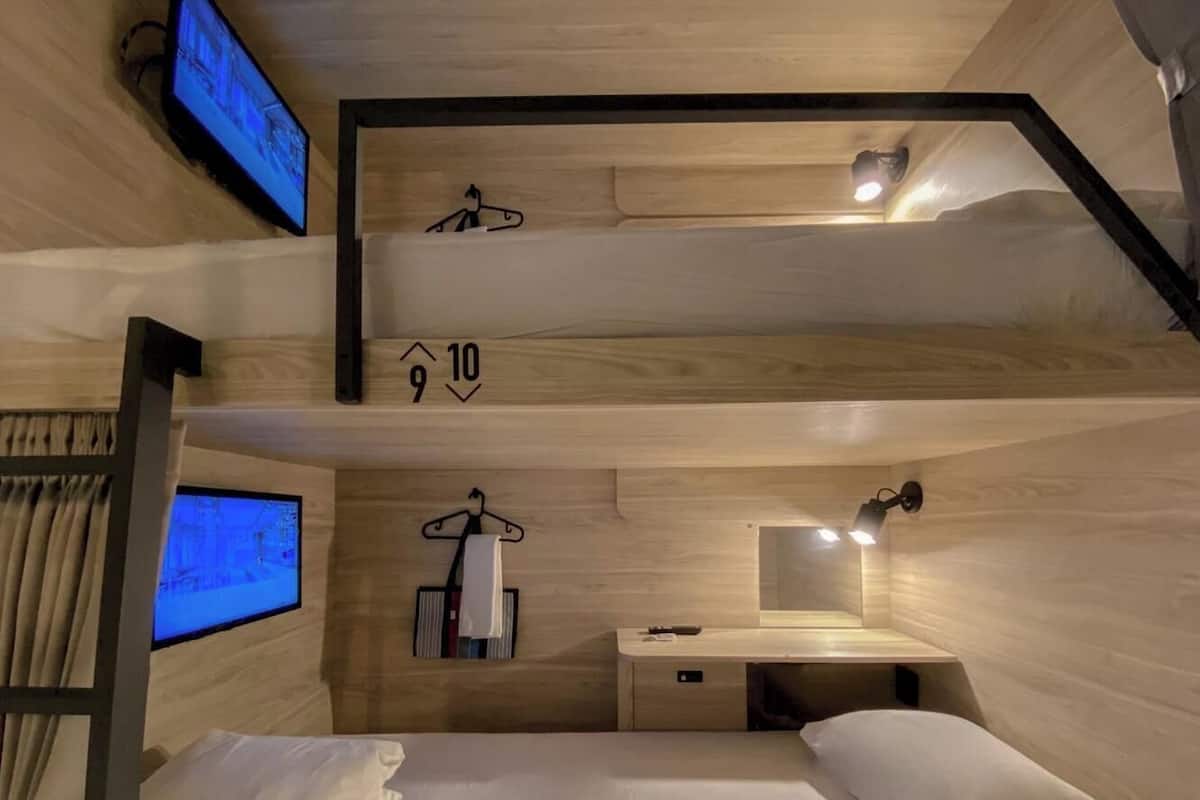 Habitación con literas, televisor, escritorio con lámpara y toallero colgante.