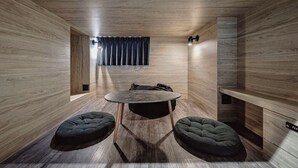 Quarto moderno com paredes de madeira, uma mesa redonda, duas poltronas de espuma, uma janela com cortinas e um banco embutido.