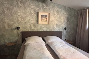 Ein Bett mit Kopfteil, zwei Nachttische, ein gerahmtes Bild an der Wand und eine Wand mit Musterpapier.