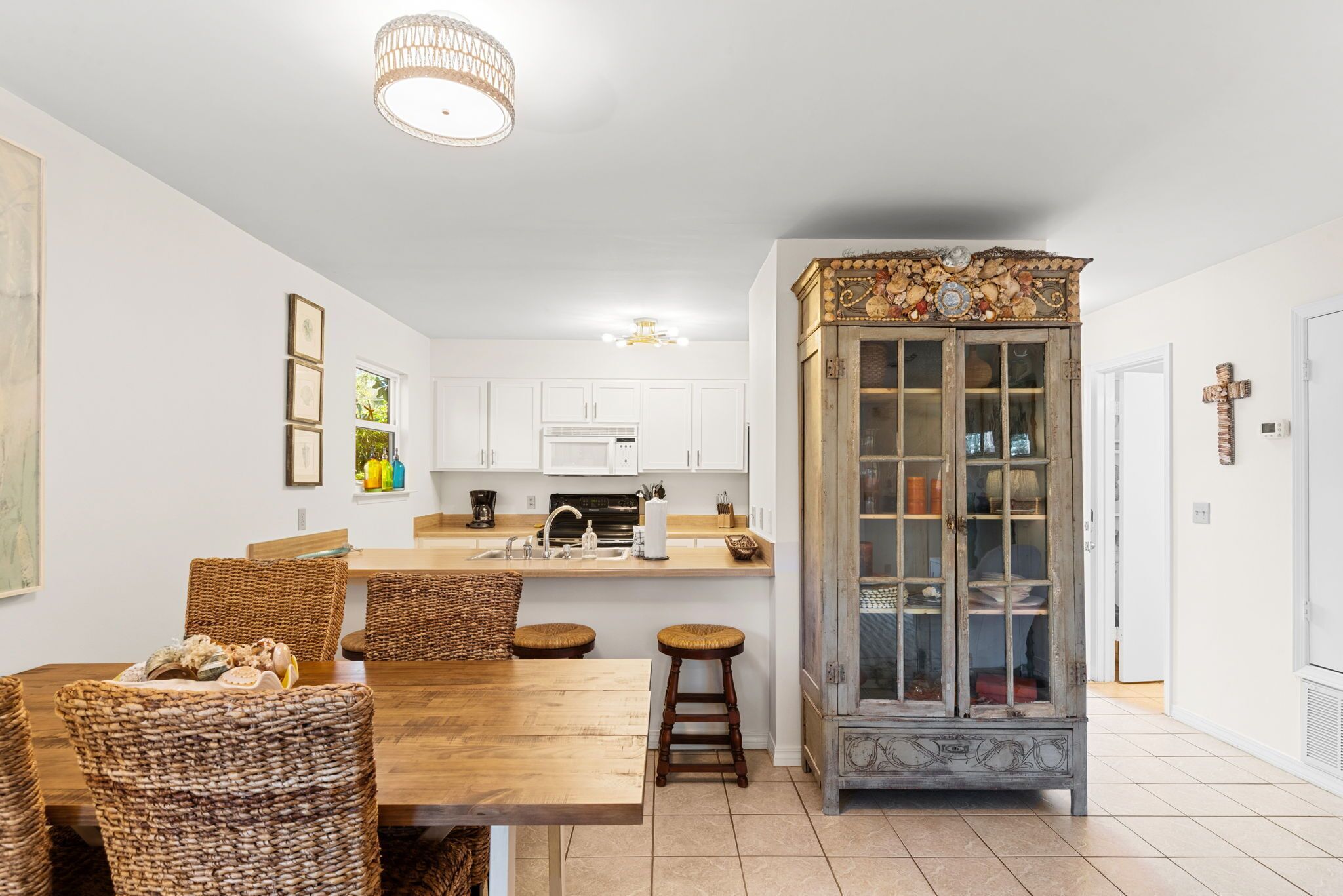 A kitchen with white cabinets, a wooden dining table with wicker chairs, and a decorative cabinet with glass doors.