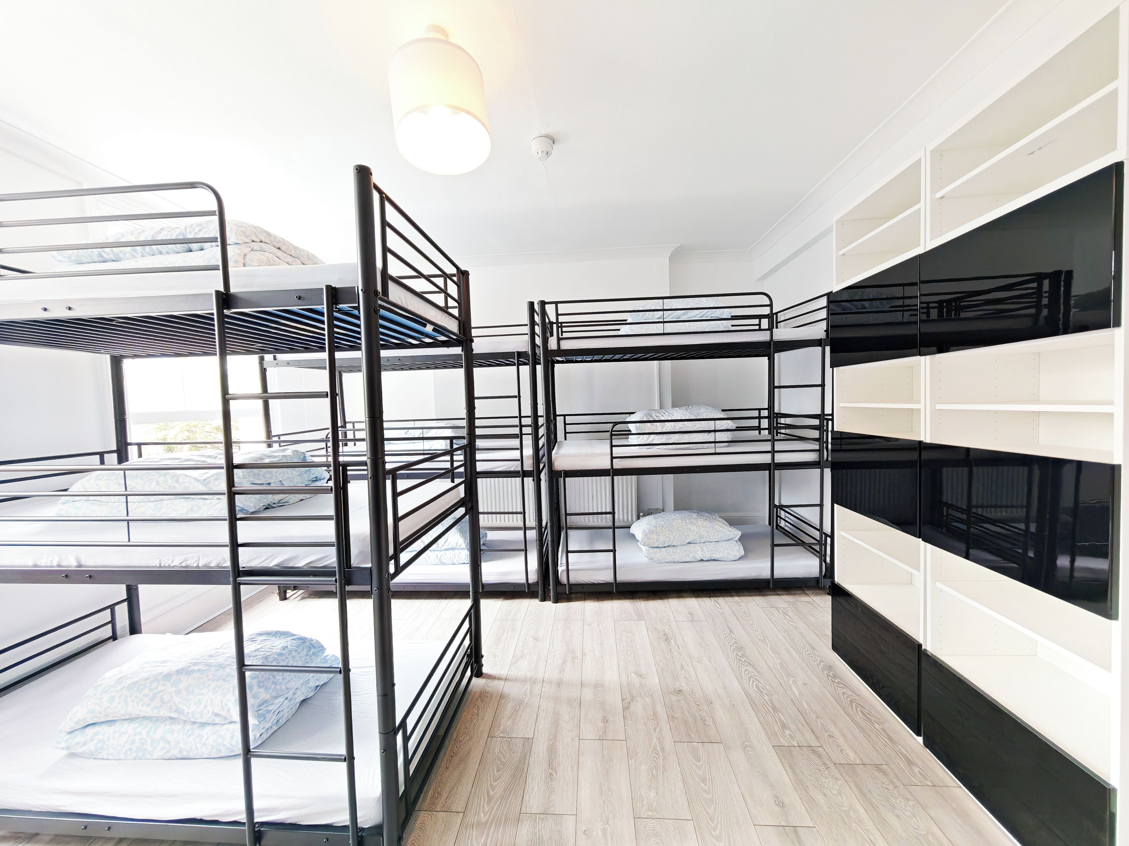 A dormitory room with bunk beds, a white wardrobe, and a wooden floor.