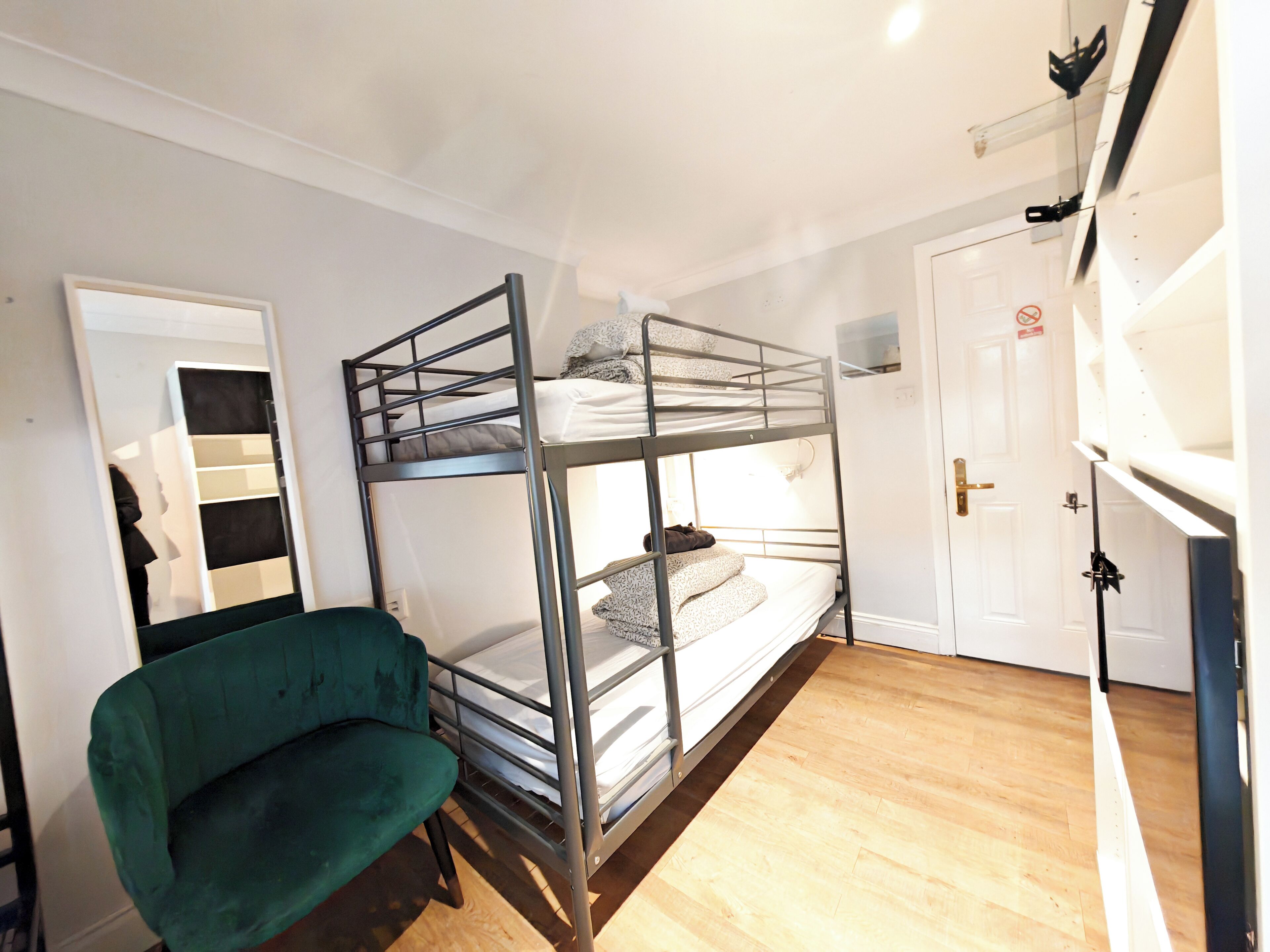 Quarto com beliche, uma cadeira verde, porta branca e chão de madeira.