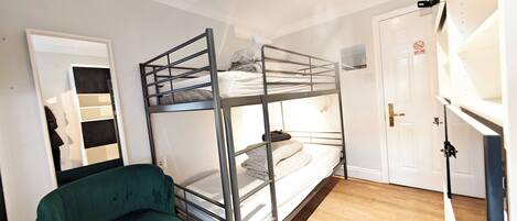 Quarto com beliche, uma cadeira verde, porta branca e chão de madeira.