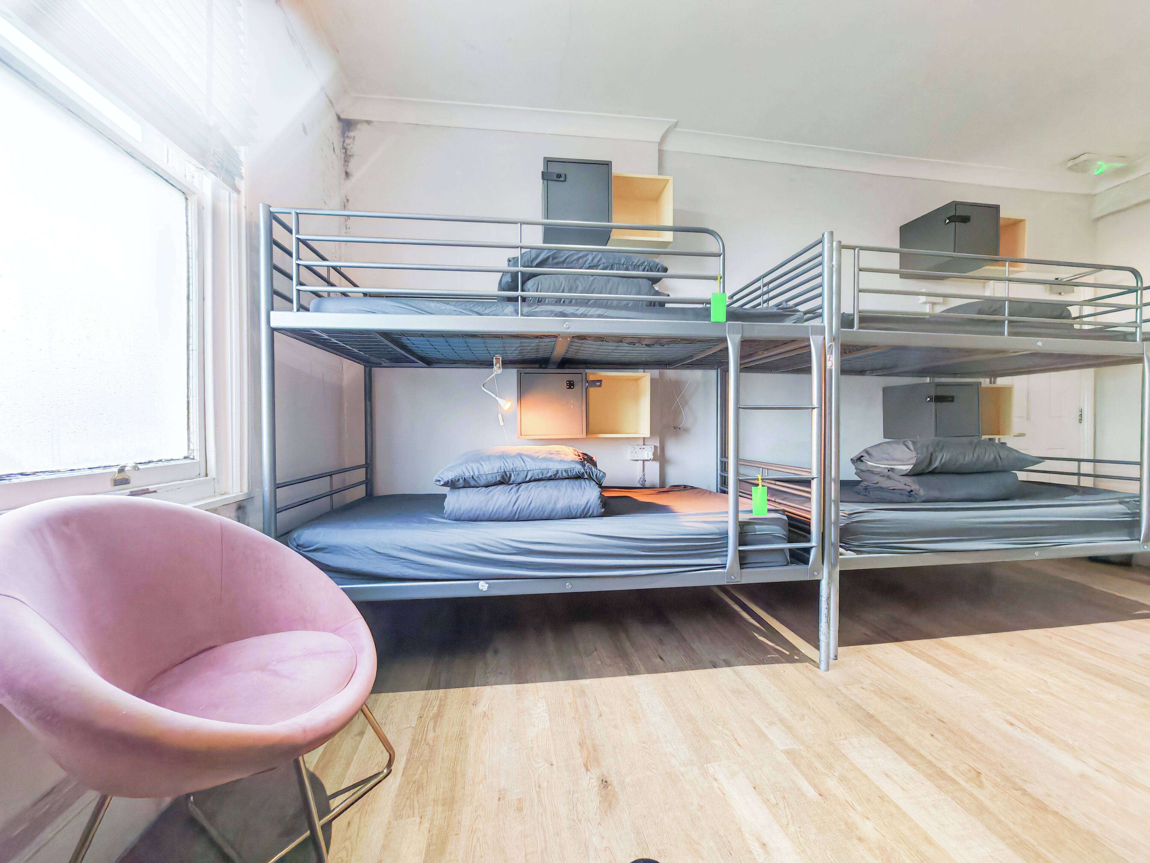A bunk bed room with a pink chair, a desk, and a window.