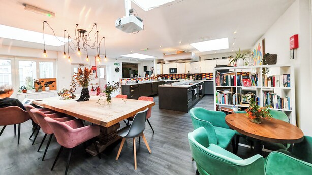 Una cocina moderna con una isla central, un comedor con sillas, una estantería y un proyector en el techo.