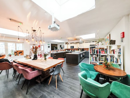 A modern kitchen with a central island, a dining area with chairs, a bookshelf, and a ceiling projector.