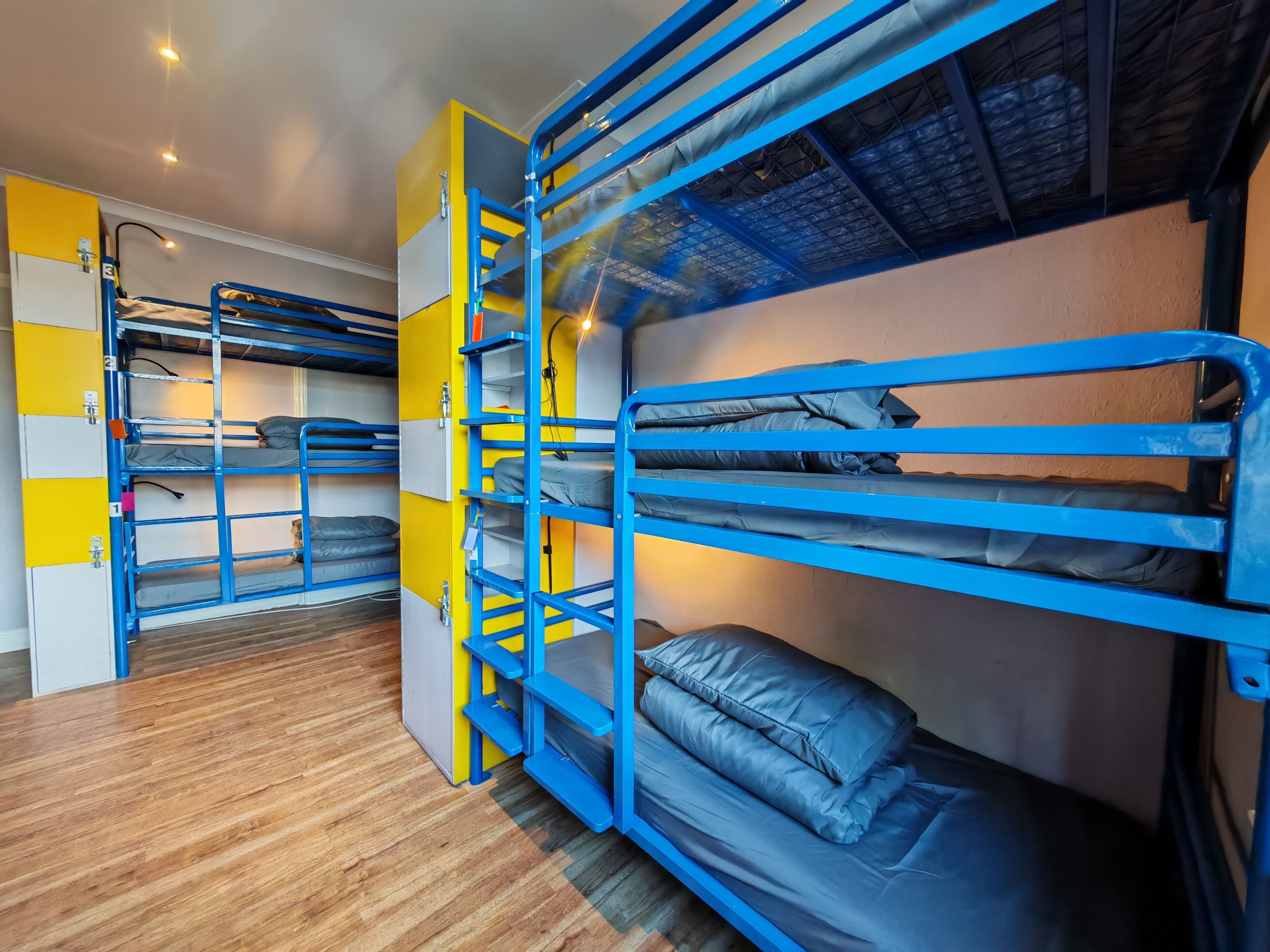 Une chambre de dortoir avec des lits superposés, un plancher en bois et une décoration aux couleurs jaune et bleu.