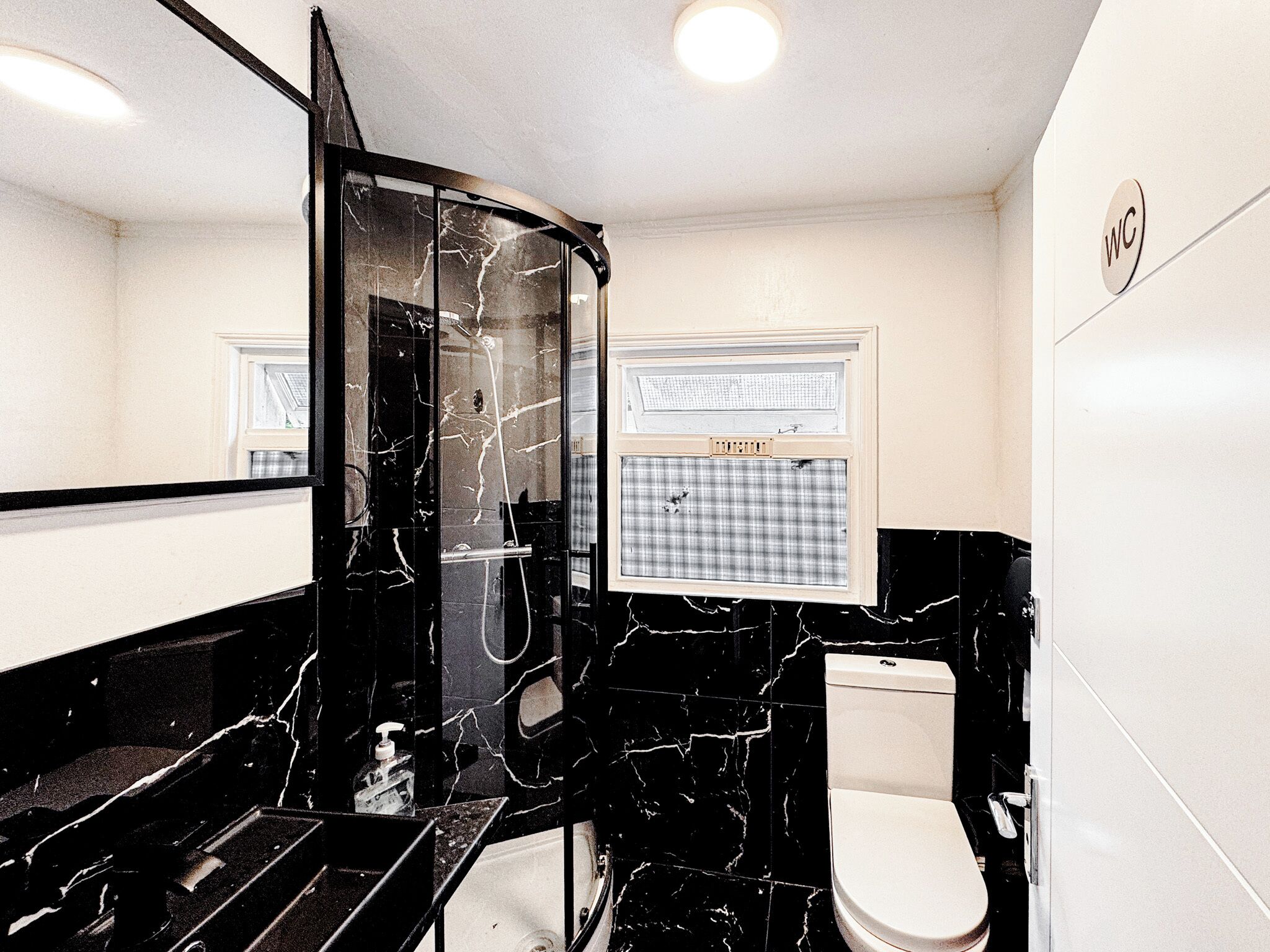 Un baño con lavamanos de mármol negro, inodoro y espejo.