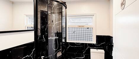 Un baño con lavamanos de mármol negro, inodoro y espejo.