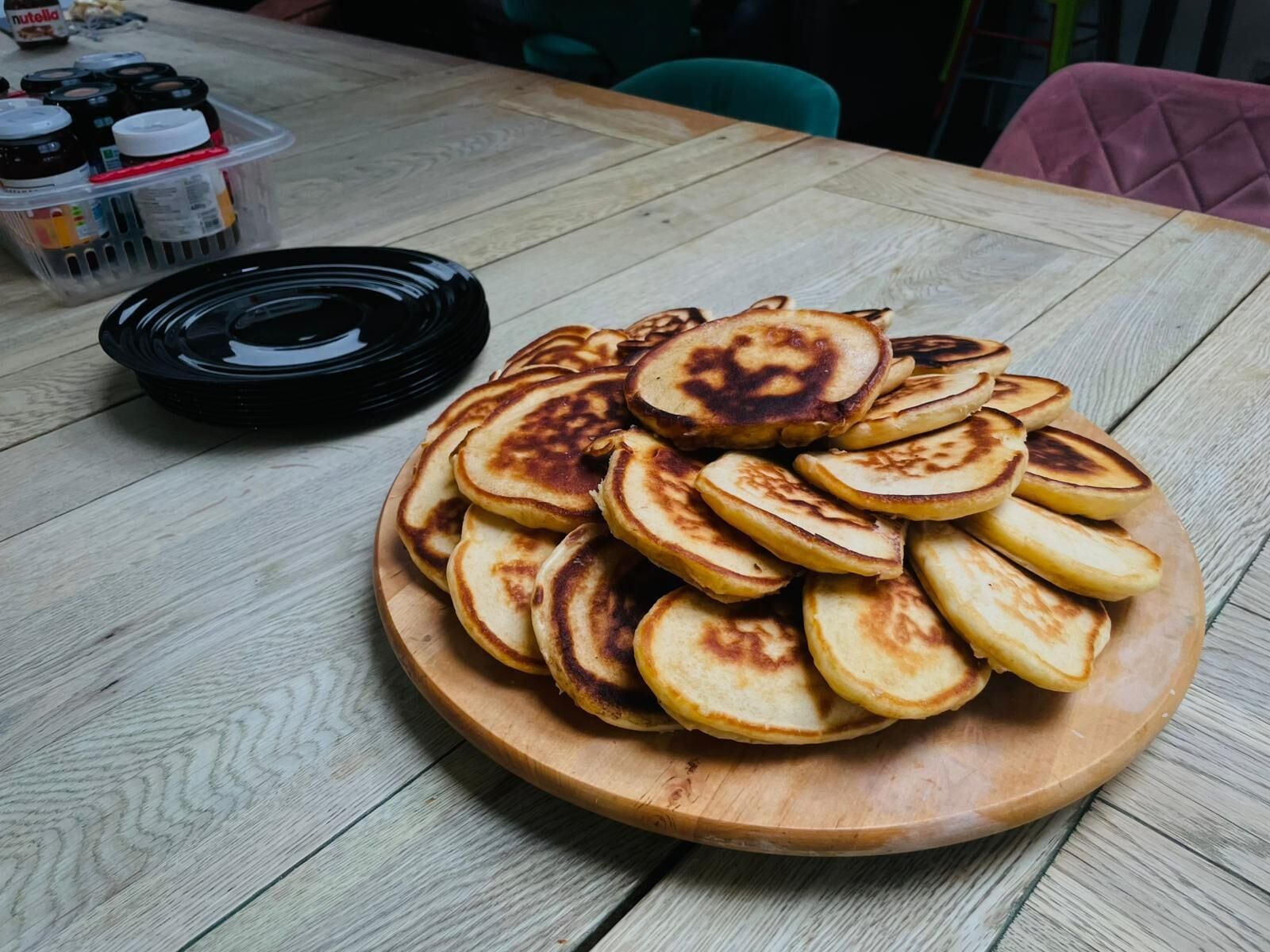 Een houten tafel met een stapel pannenkoeken en een zwart bord ernaast.