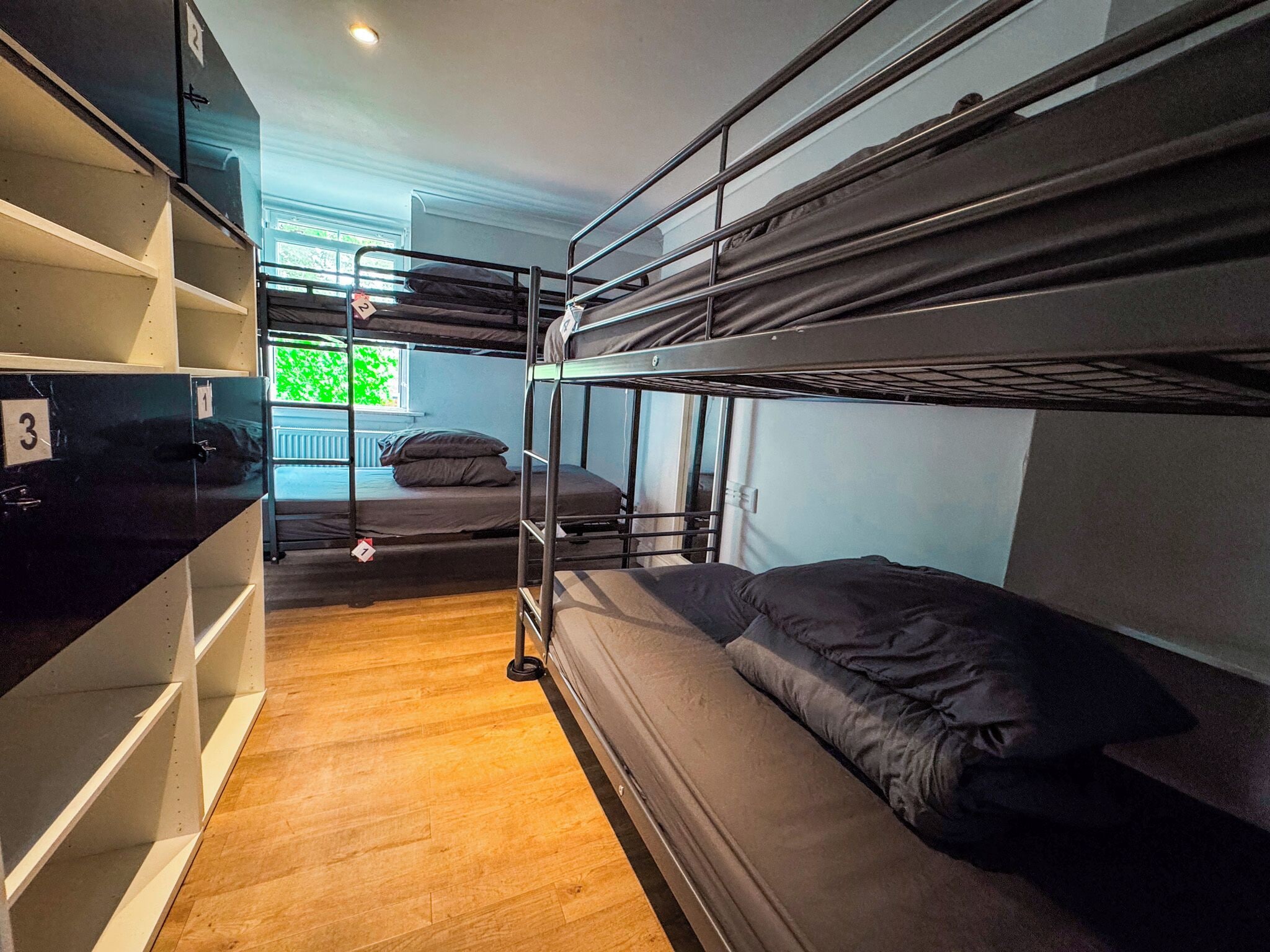 A bunk bed room with a wooden floor, metal bunk beds, and a shelving unit with numbered compartments.