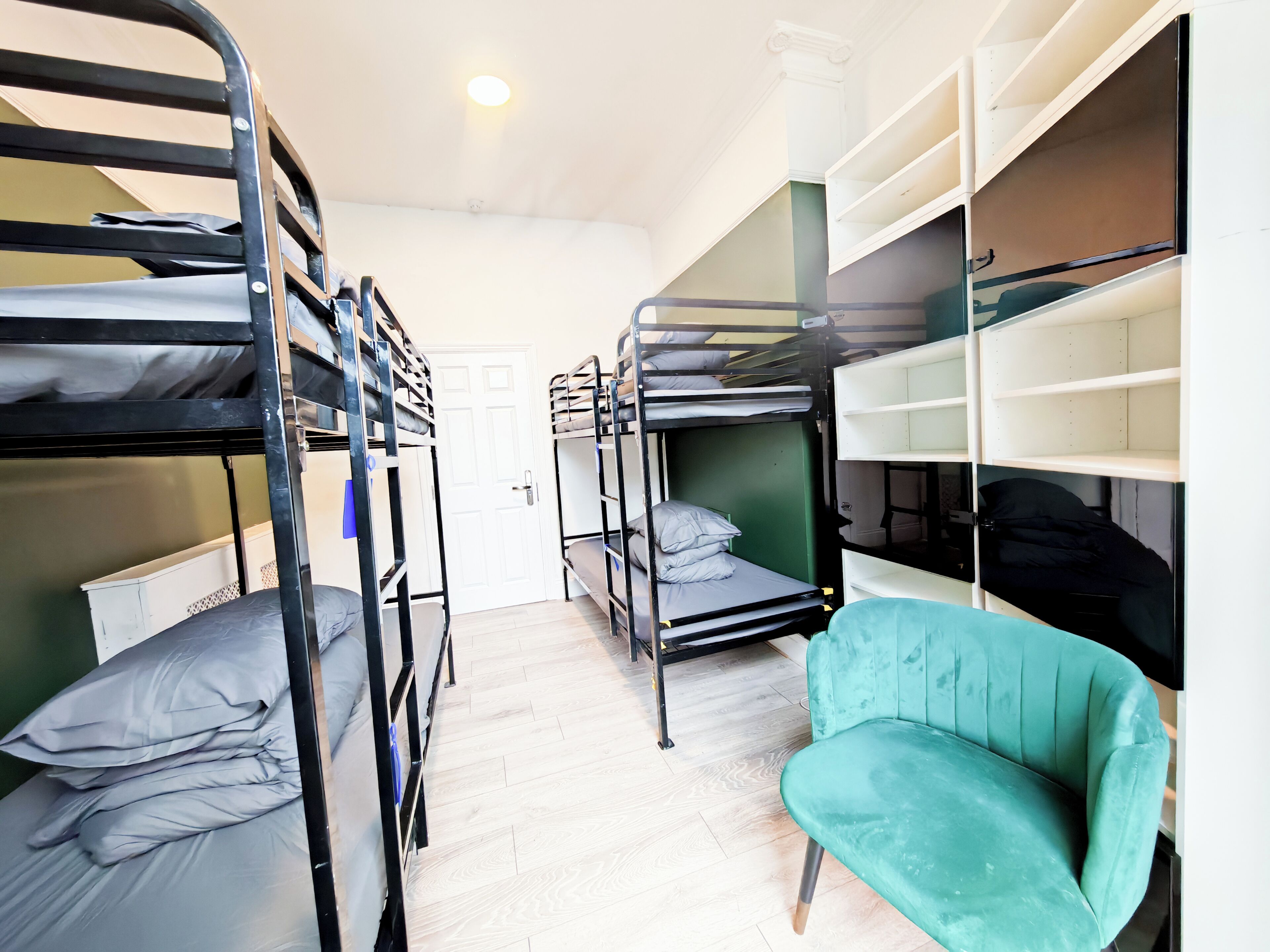 Une chambre avec des lits superposés, un fauteuil de couleur turquoise et des étagères intégrées.