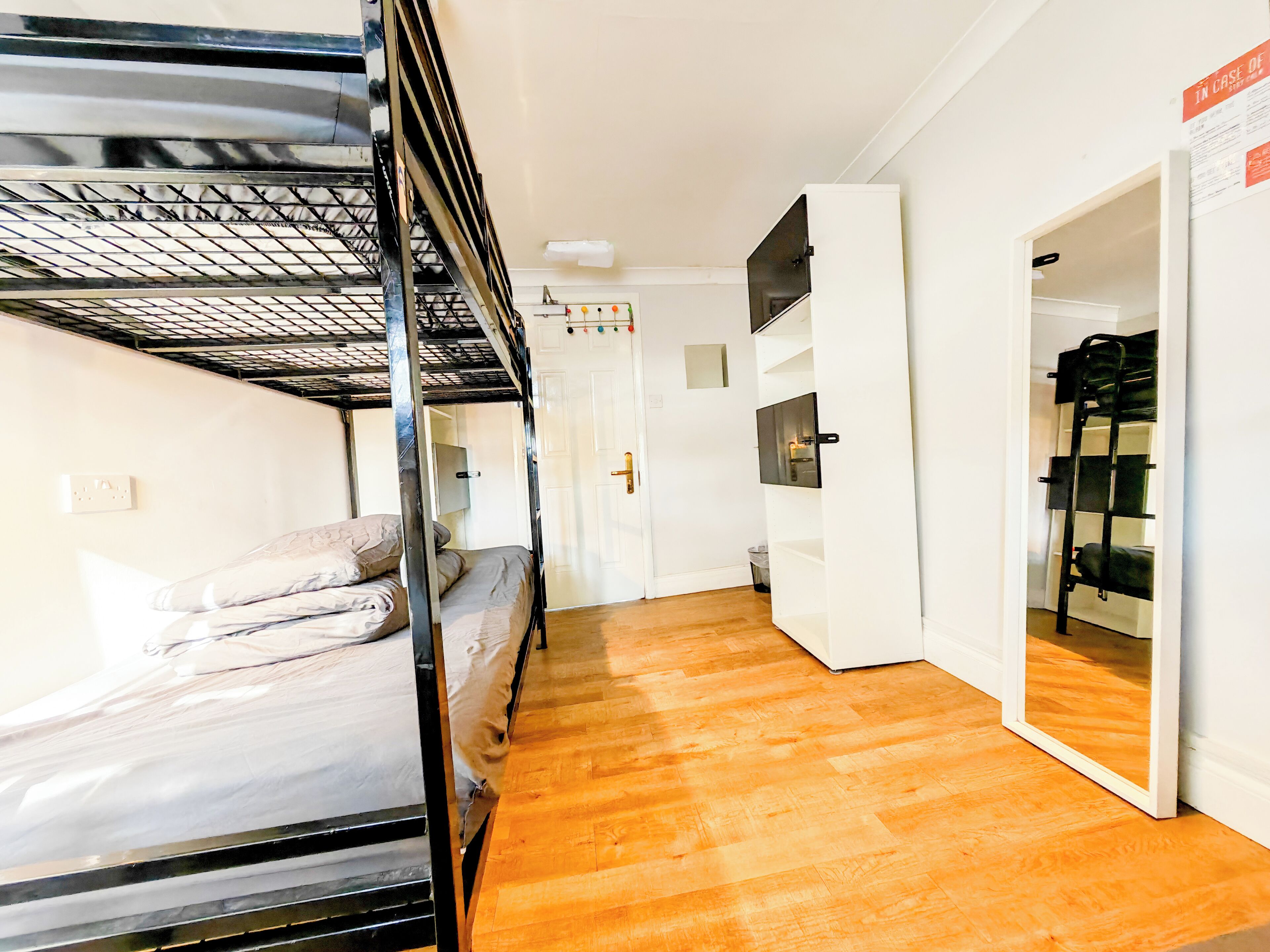 Um quarto com uma cama beliche, uma porta branca, um espelho e piso de madeira.