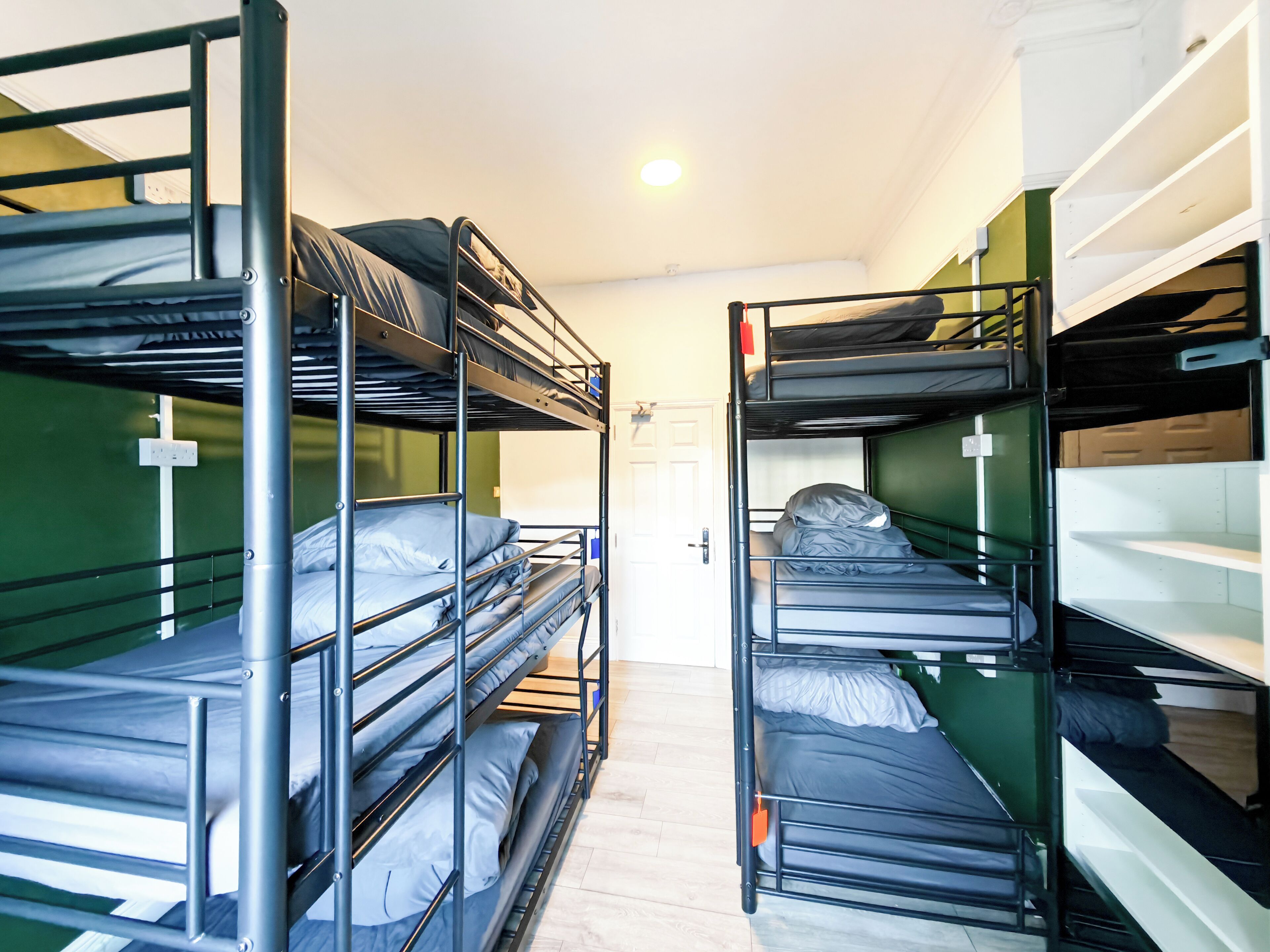 A dormitory room with bunk beds, a door, and a light fixture.