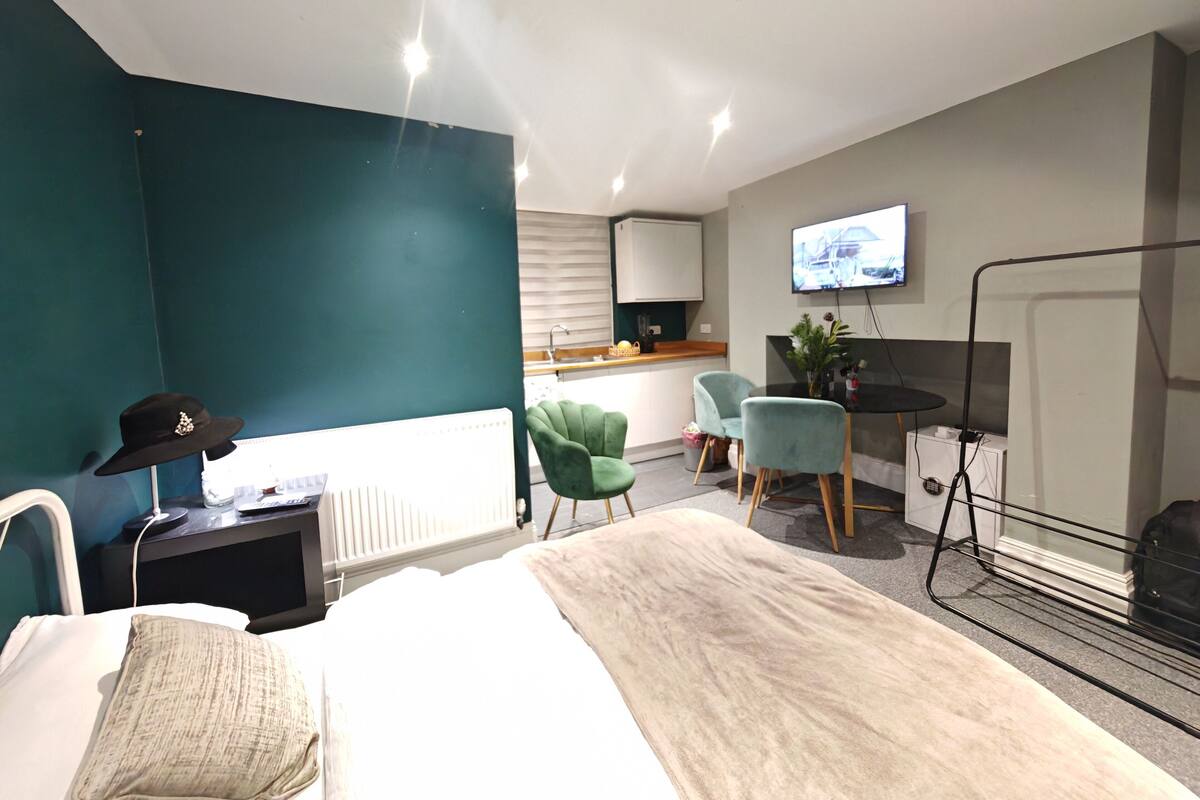 Moderni hotellihuone, jossa on sänky, työpöytä, kaksi tuolia, televisio ja patteri.