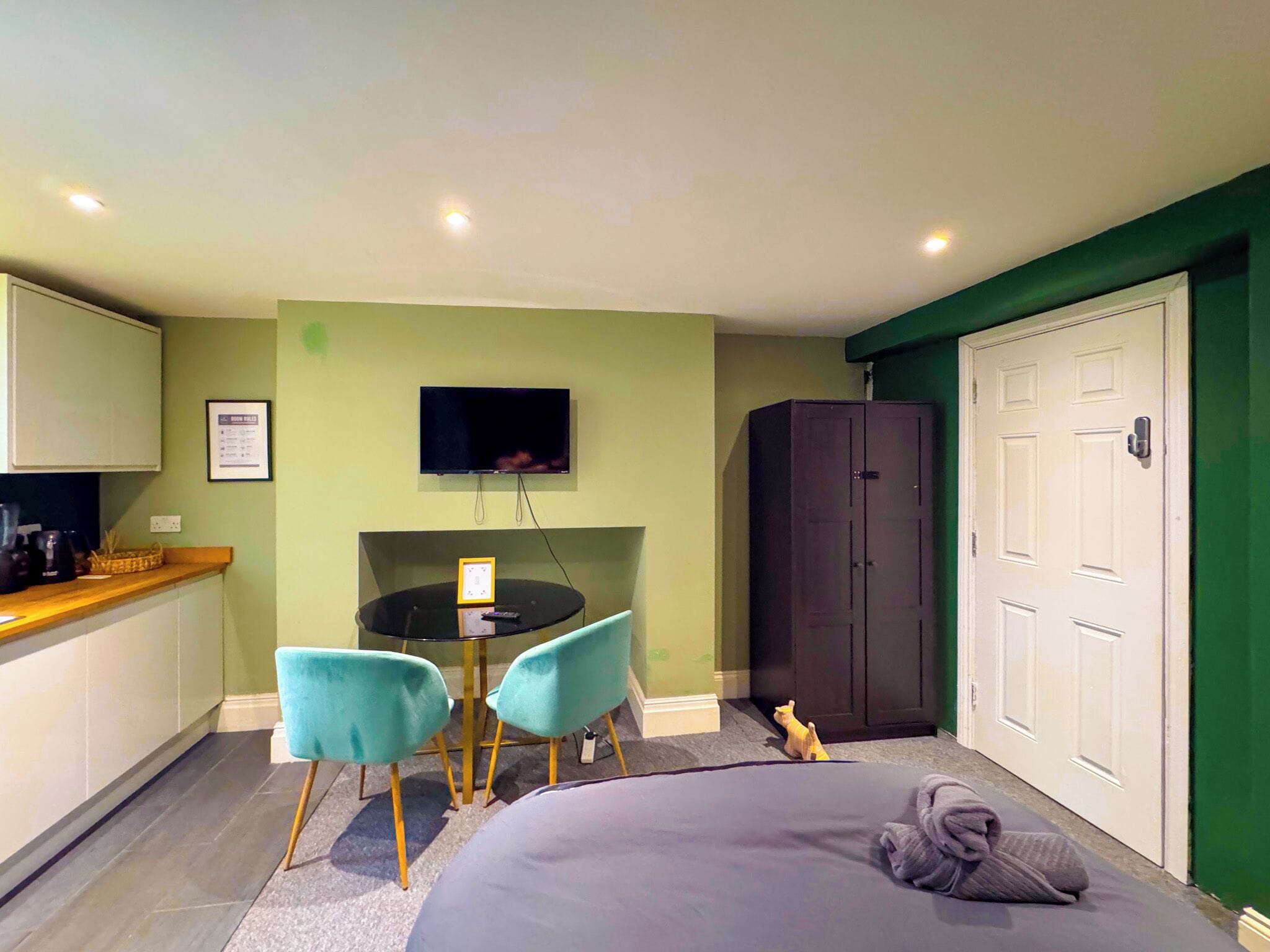 A room with a bed, a desk with two chairs, a television on the wall, and a wardrobe.