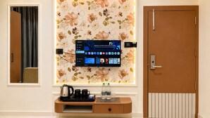 A hotel room with a flat-screen TV mounted on a floral wallpaper, a coffee maker, water bottles, and a door with a handle. - Velar Prime Hotel, Vijay Nagar, Indore (Indore)