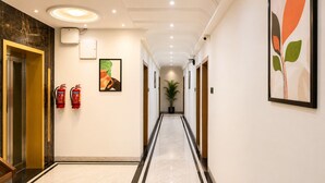 A hotel hallway with a marble floor, fire extinguishers, framed artwork, and a potted plant. - Velar Prime Hotel, Vijay Nagar, Indore (Indore)