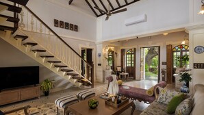 A spacious living area with a staircase, a sofa set, a coffee table, and a television. - Staymaster Samba Sunset 3BR Pvt Pool (Anjuna)
