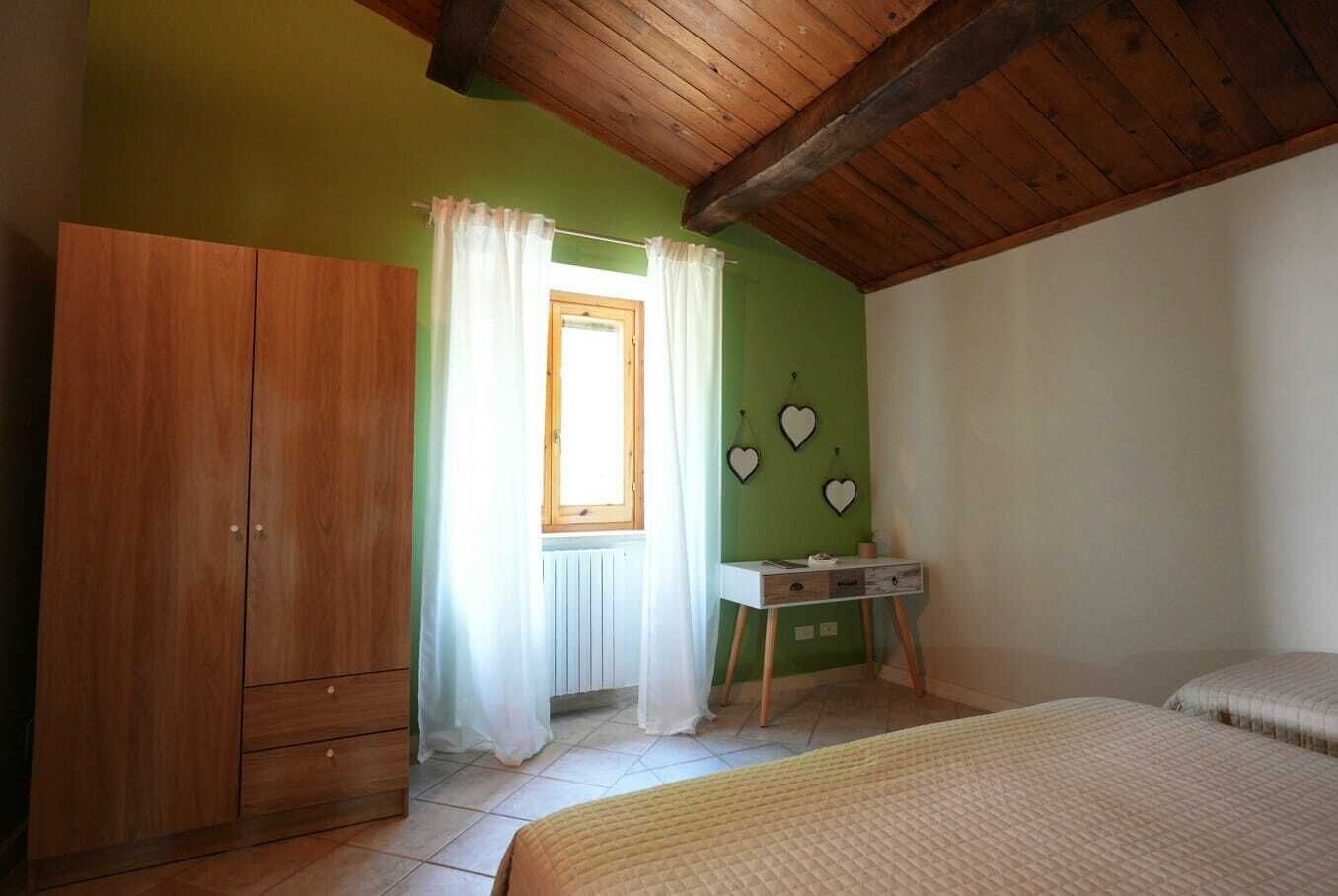 Une chambre avec une armoire en bois, une table de chevet, une fenêtre avec des rideaux et des décorations murales en forme de cœur.