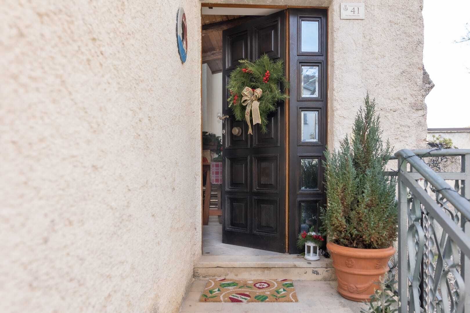 A door with a wreath, a potted plant, and a doormat.